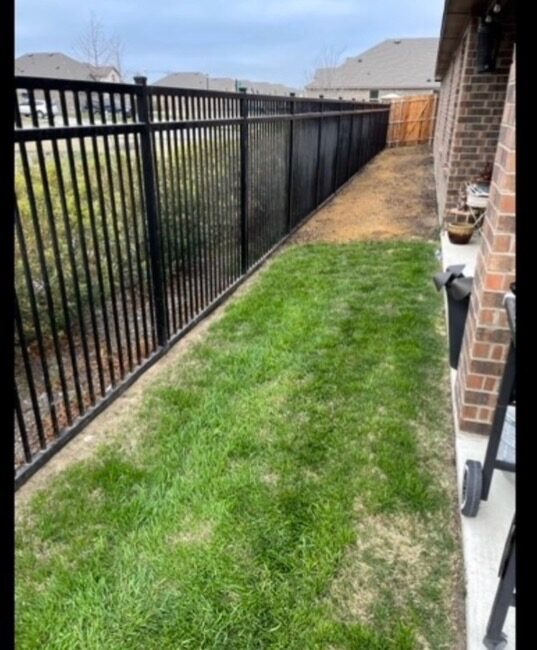 Ornamental iron fence with fresh sod along a side yard